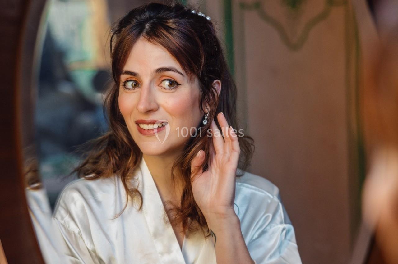 Femme en robe de satin blanche se regardant dans un miroir tout en ajustant une boucle d'oreille.