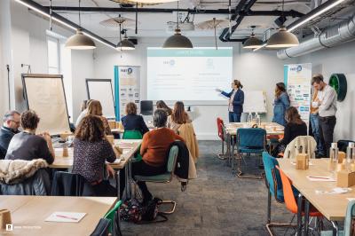 Des personnes assistent à une présentation dans une salle moderne avec un écran affichant un ordre du jour.