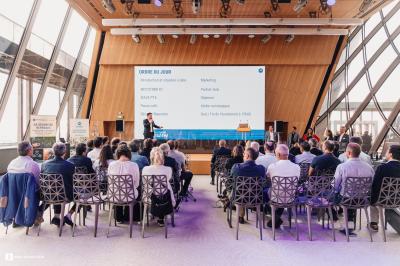 Des personnes assistent à une présentation dans une salle moderne avec un écran affichant un ordre du jour.