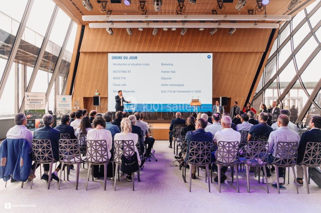 Des personnes assistent à une présentation dans une salle moderne avec un écran affichant un ordre du jour.