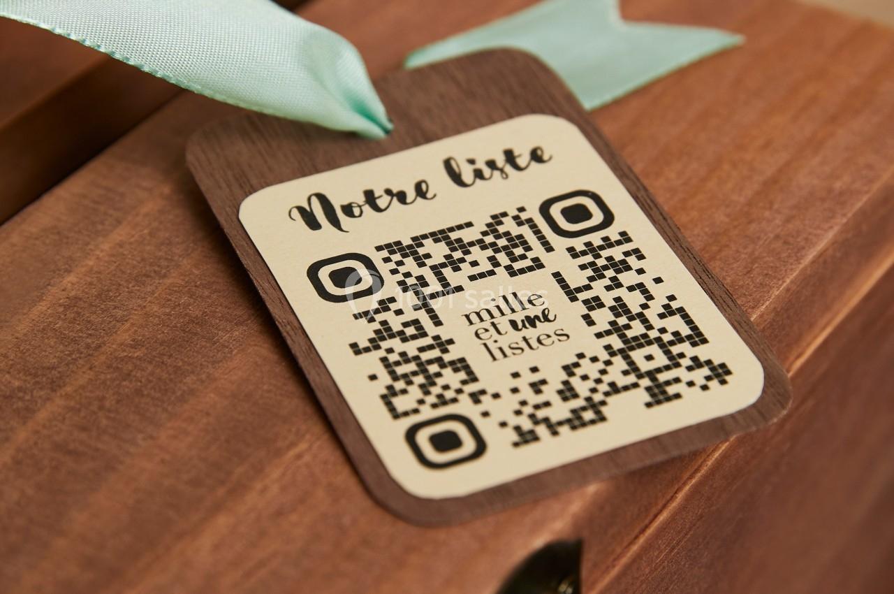 Étiquette en bois avec un QR code et l'inscription ’Notre liste’, attachée à un ruban vert sur une surface en bois.