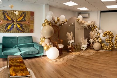 Espace salon chaleureux avec mobilier en bois, coussins rouges, plantes vertes et lumière naturelle entrant par le toit.