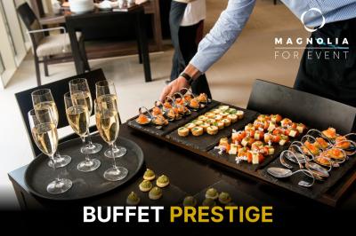 Salon lumineux avec mobilier en bois, plantes vertes, canapés, table basse et cuisine ouverte en arrière-plan.