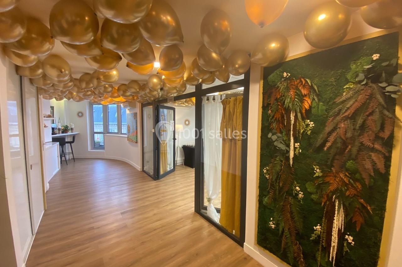 Plafond décoré de ballons dorés, mur végétal et sol en bois dans un espace lumineux avec des baies vitrées.