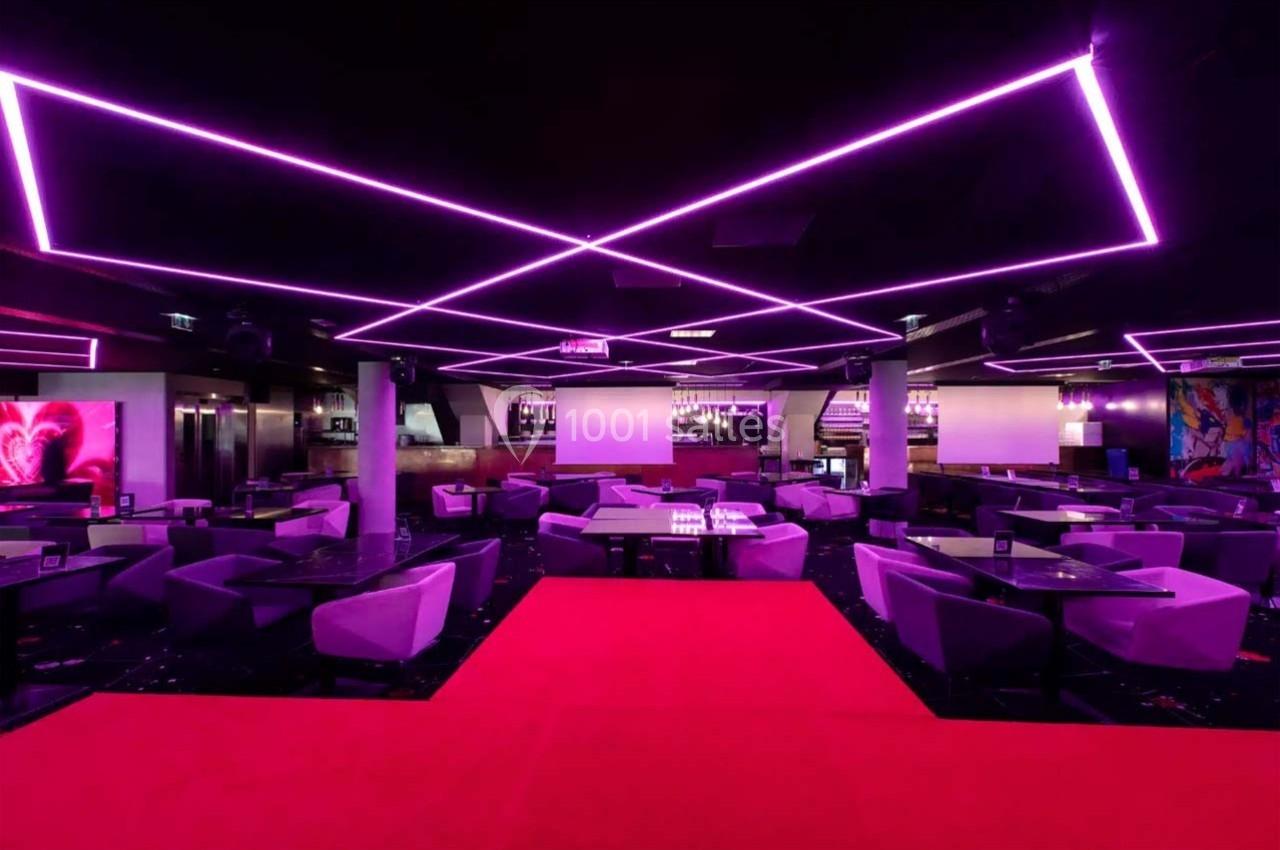 Salle de réception moderne avec éclairage néon violet, tables, fauteuils et tapis rouge au centre.