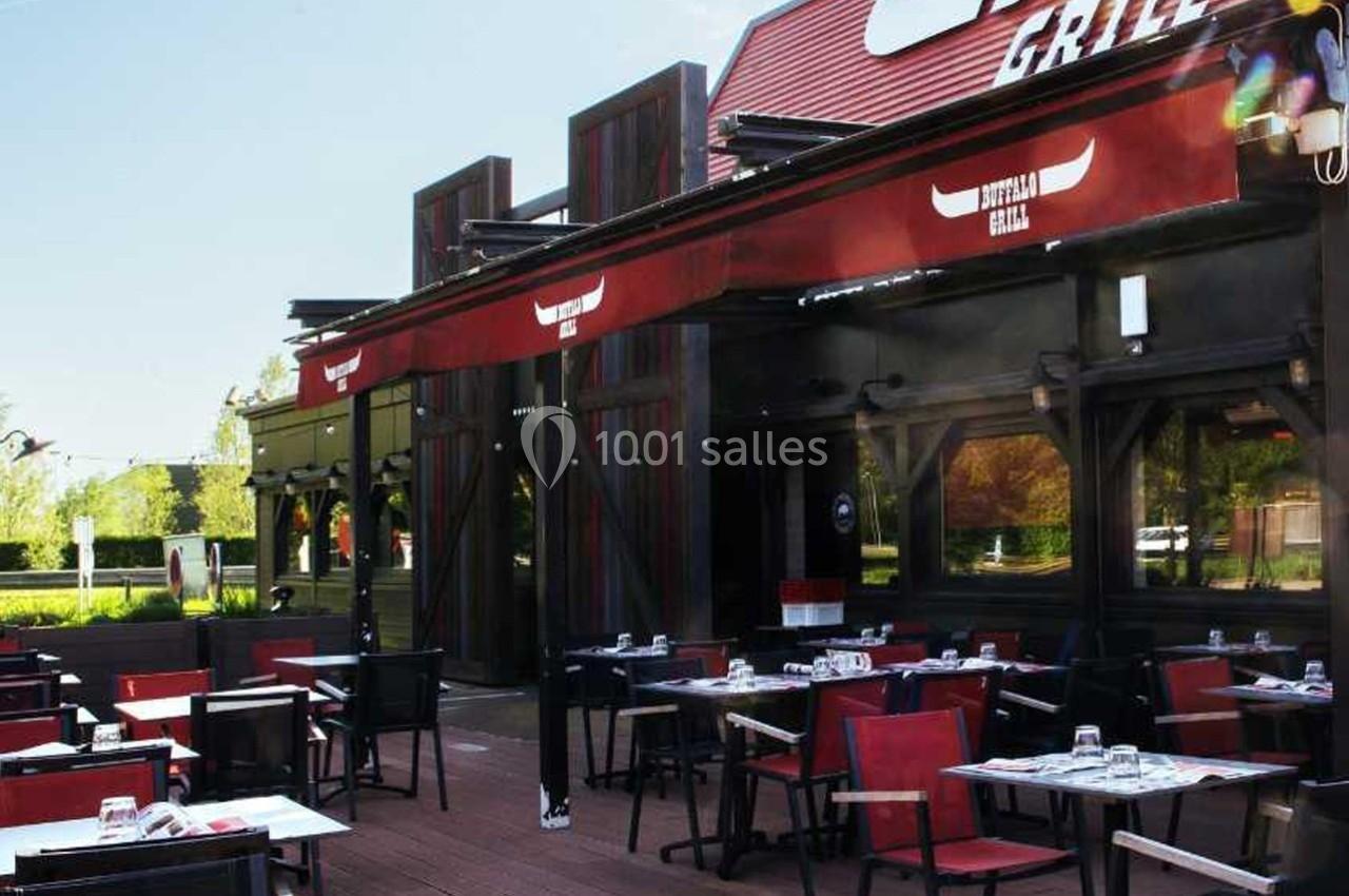 Terrasse d'un restaurant avec tables dressées, chaises rouges et noires, et auvent rouge sous un ciel dégagé.