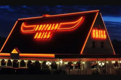 Entrée d'un restaurant avec une enseigne ’Buffalo Grill’ et une porte vitrée affichant des autocollants.