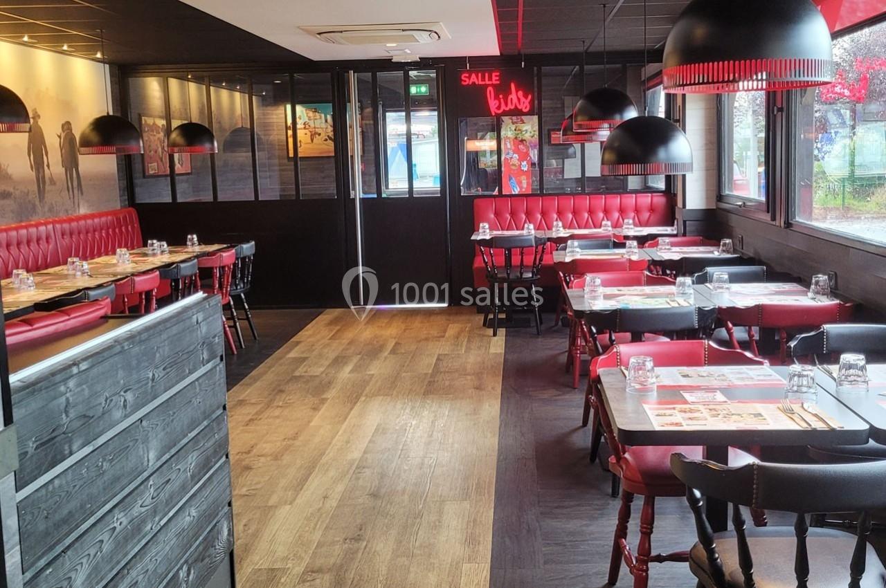 Salle de restaurant avec tables dressées, banquettes rouges, chaises noires et grandes suspensions lumineuses.