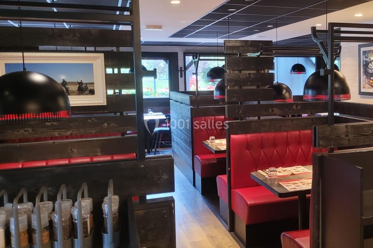 Salle de restaurant avec banquettes rouges, cloisons en bois sombre et luminaires suspendus noirs.