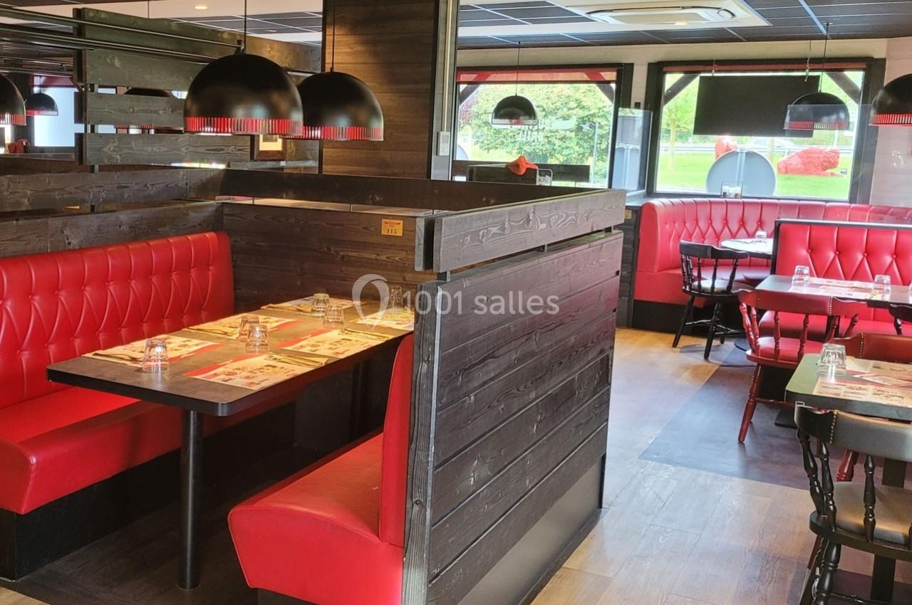Salle de restaurant avec banquettes rouges, tables dressées et luminaires suspendus dans un décor en bois sombre.