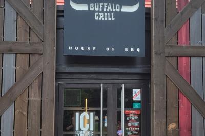 Entrée d'un restaurant avec une enseigne ’Buffalo Grill’ et une porte vitrée affichant des autocollants.