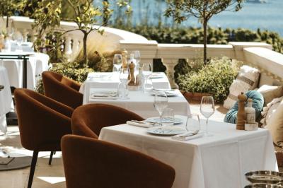 Un homme souriant partage un repas en terrasse avec d'autres personnes, entouré de plats variés et d'un décor extérieur.