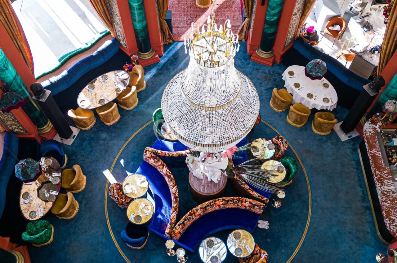 Vue aérienne d'une salle de restaurant élégante avec un grand lustre central, des tables rondes et une décoration colorée.