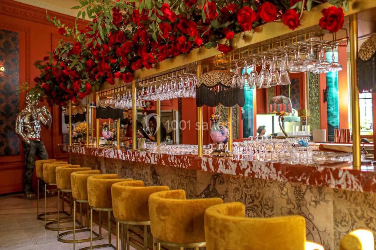 Bar élégant avec tabourets jaunes, comptoir décoré, verrerie suspendue et ornements de roses rouges.