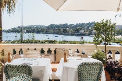 Un homme souriant partage un repas en terrasse, entouré de plats variés et d'une vue sur un paysage ensoleillé.