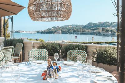 Un homme souriant partage un repas en terrasse, entouré de plats variés et d'une vue sur un paysage ensoleillé.