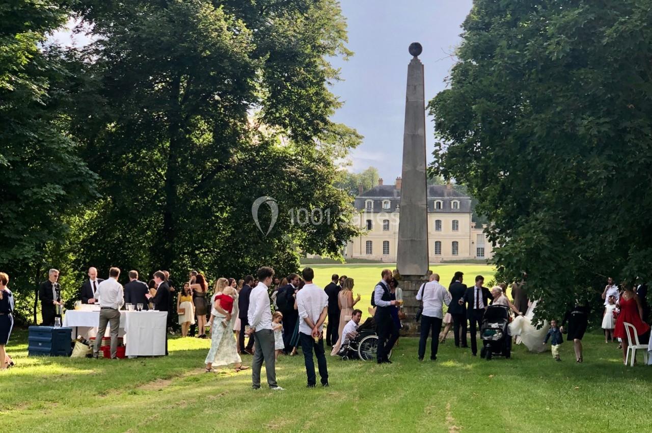 Groupe de personnes rassemblées dans un parc verdoyant près d'un obélisque, avec un château en arrière-plan.