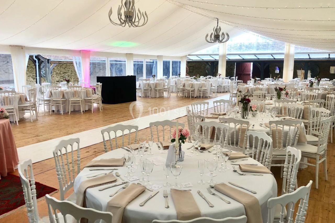 Salle de réception décorée avec des tables rondes dressées, nappes blanches, chaises élégantes et éclairage chaleureux.
