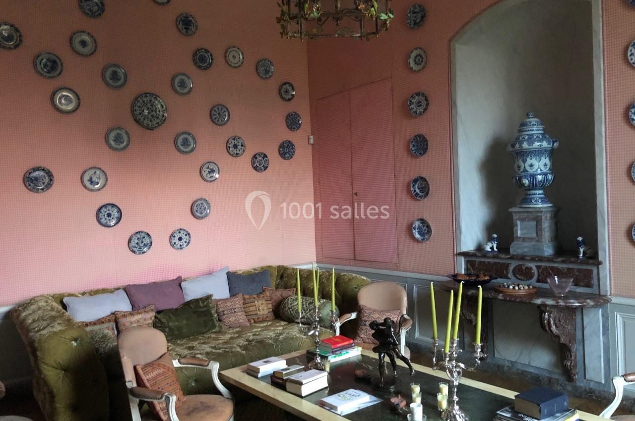 Salon avec murs roses décorés d'assiettes, canapé en velours, table basse avec chandeliers et urne en céramique sur une…
