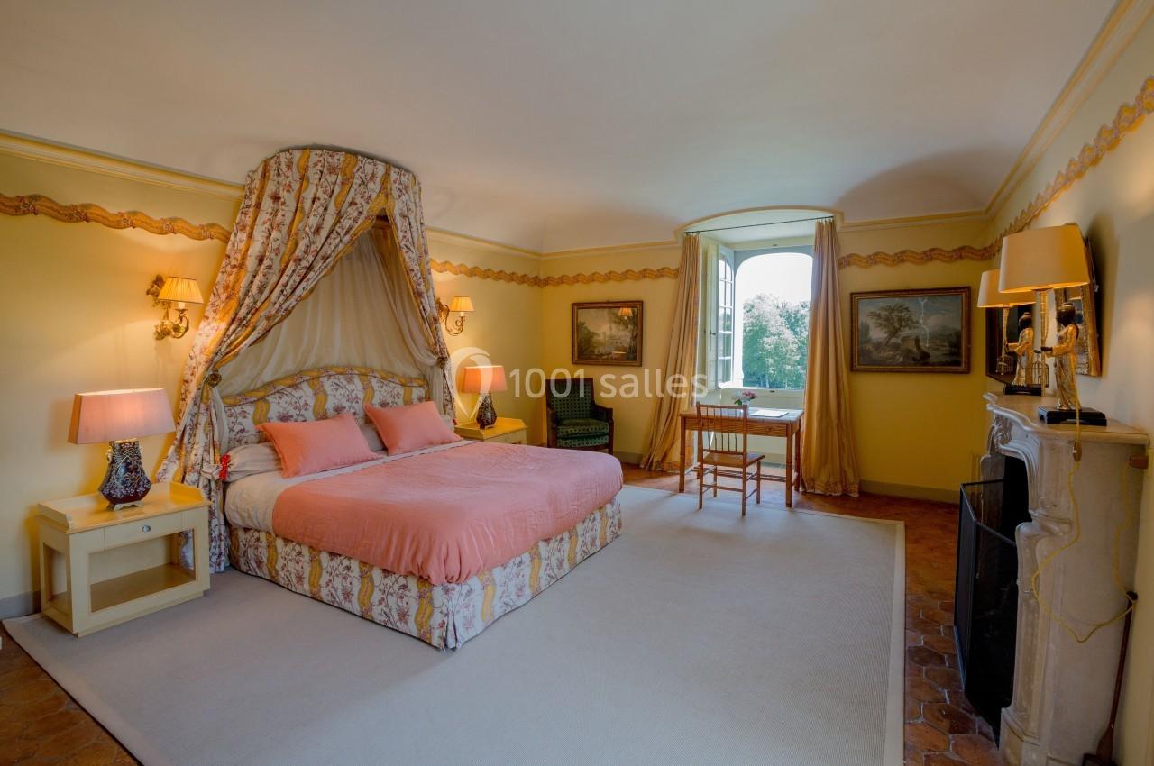 Chambre lumineuse avec lit à baldaquin, murs jaunes, mobilier classique et fenêtre donnant sur un paysage verdoyant.