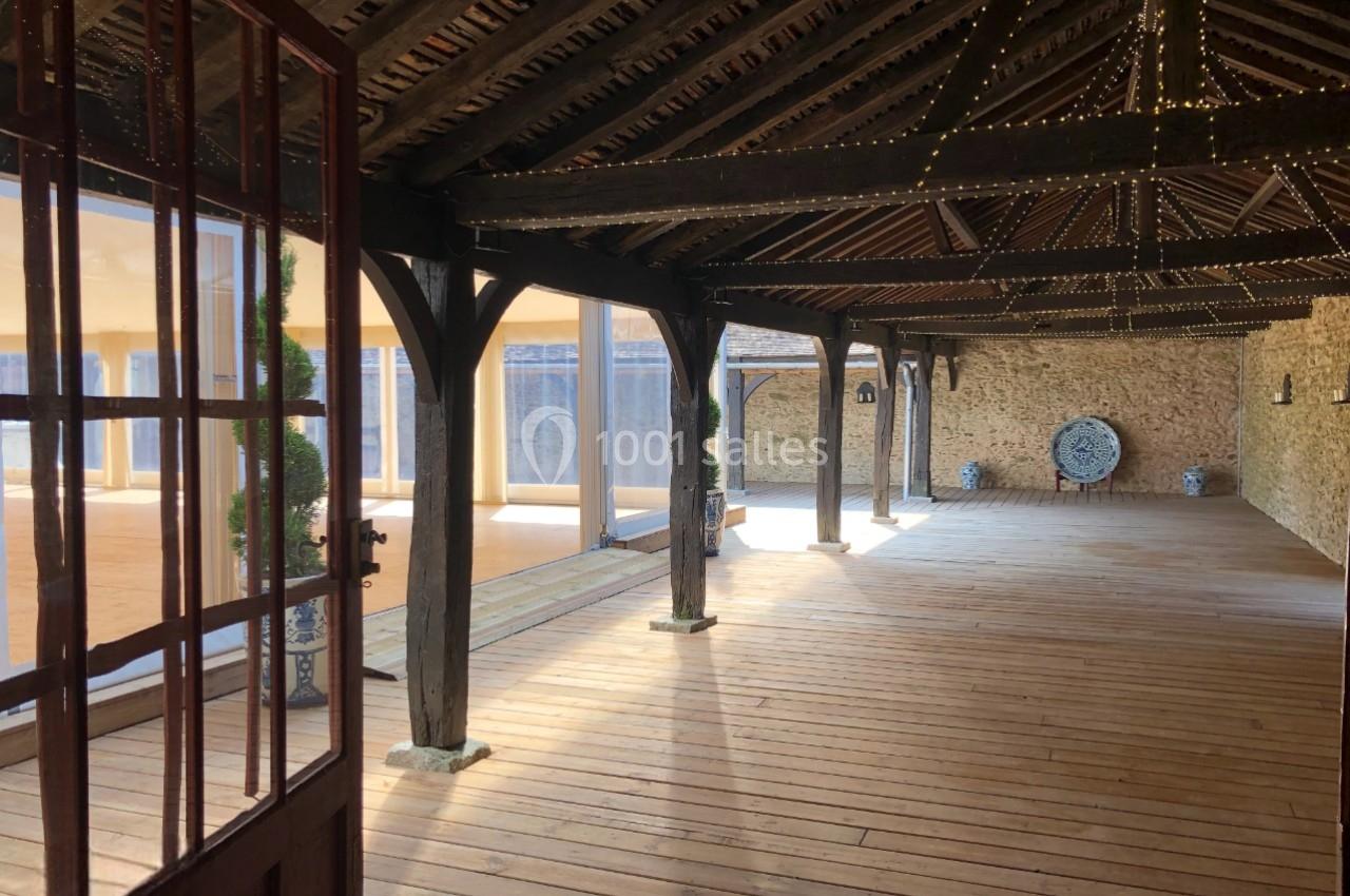 Salle en bois avec poutres apparentes, éclairée par des guirlandes lumineuses et ouverte sur une cour extérieure.