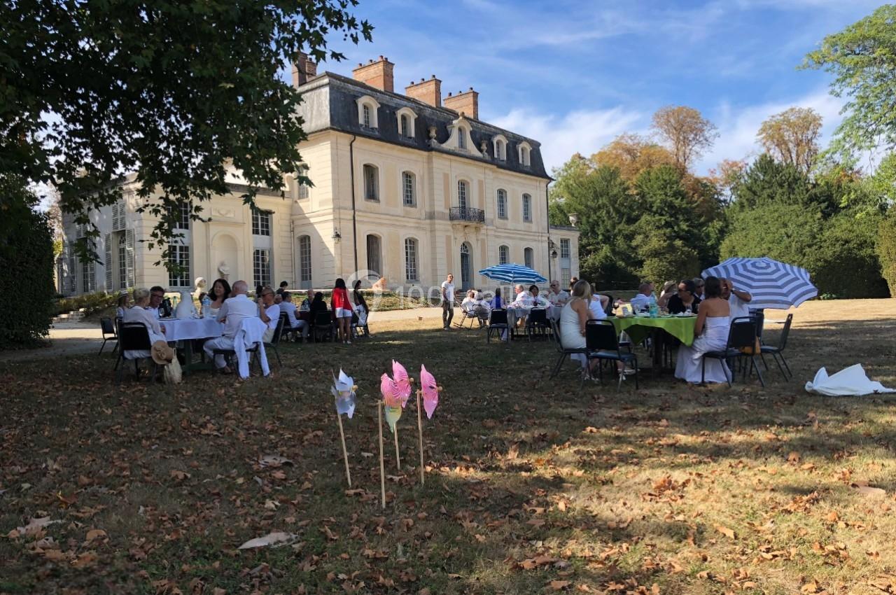 Des personnes assises à des tables en plein air devant un grand bâtiment ancien entouré d'arbres.