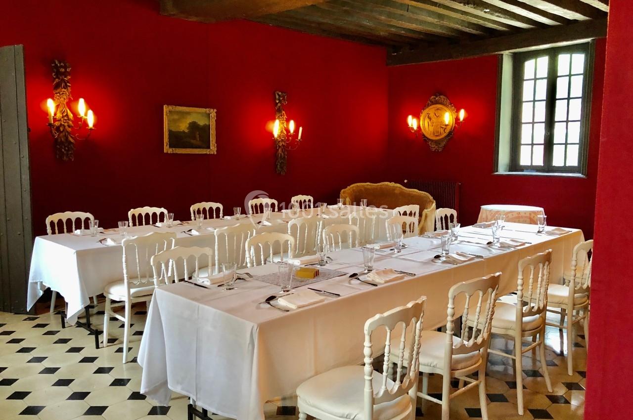 Salle à manger élégante avec murs rouges, tables dressées avec nappes blanches et chaises blanches, éclairage chaleureux.