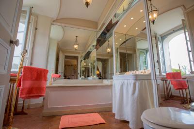 Salle de bain lumineuse avec baignoire, lavabo fleuri, miroirs, serviettes rouges et plafond peint en ciel nuageux.