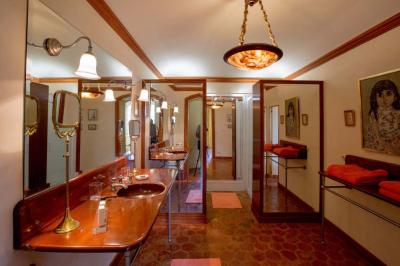 Salle de bain lumineuse avec baignoire, lavabo fleuri, miroirs, serviettes rouges et plafond peint en ciel nuageux.