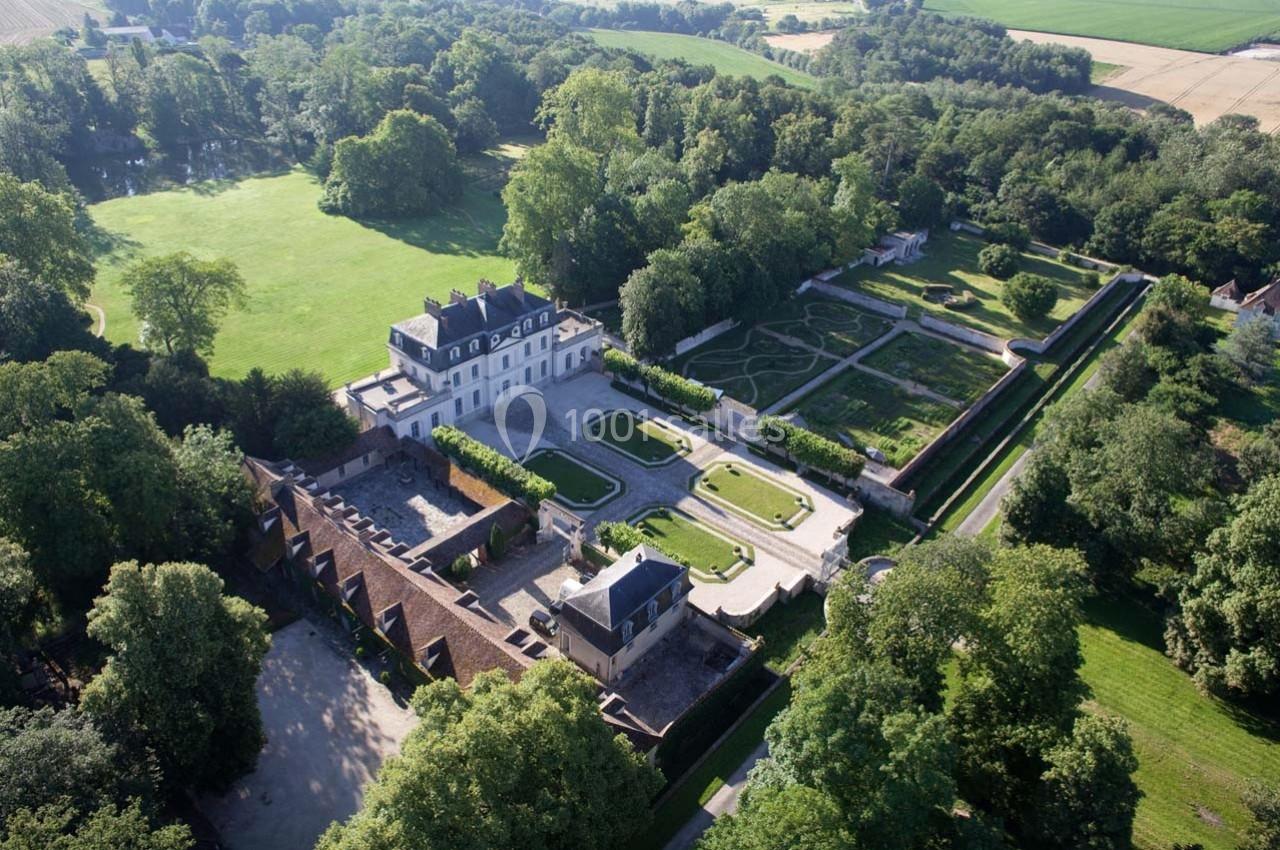 Vue aérienne d'un château entouré de jardins symétriques, d'arbres et de vastes espaces verts en campagne.