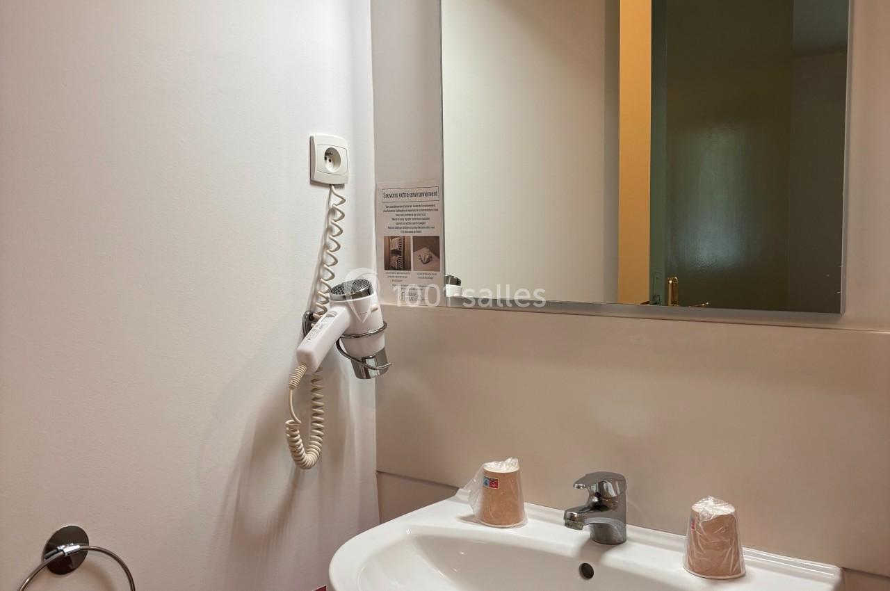 Lavabo blanc avec miroir éclairé, sèche-cheveux mural et serviette accrochée, dans une salle de bain sobre.