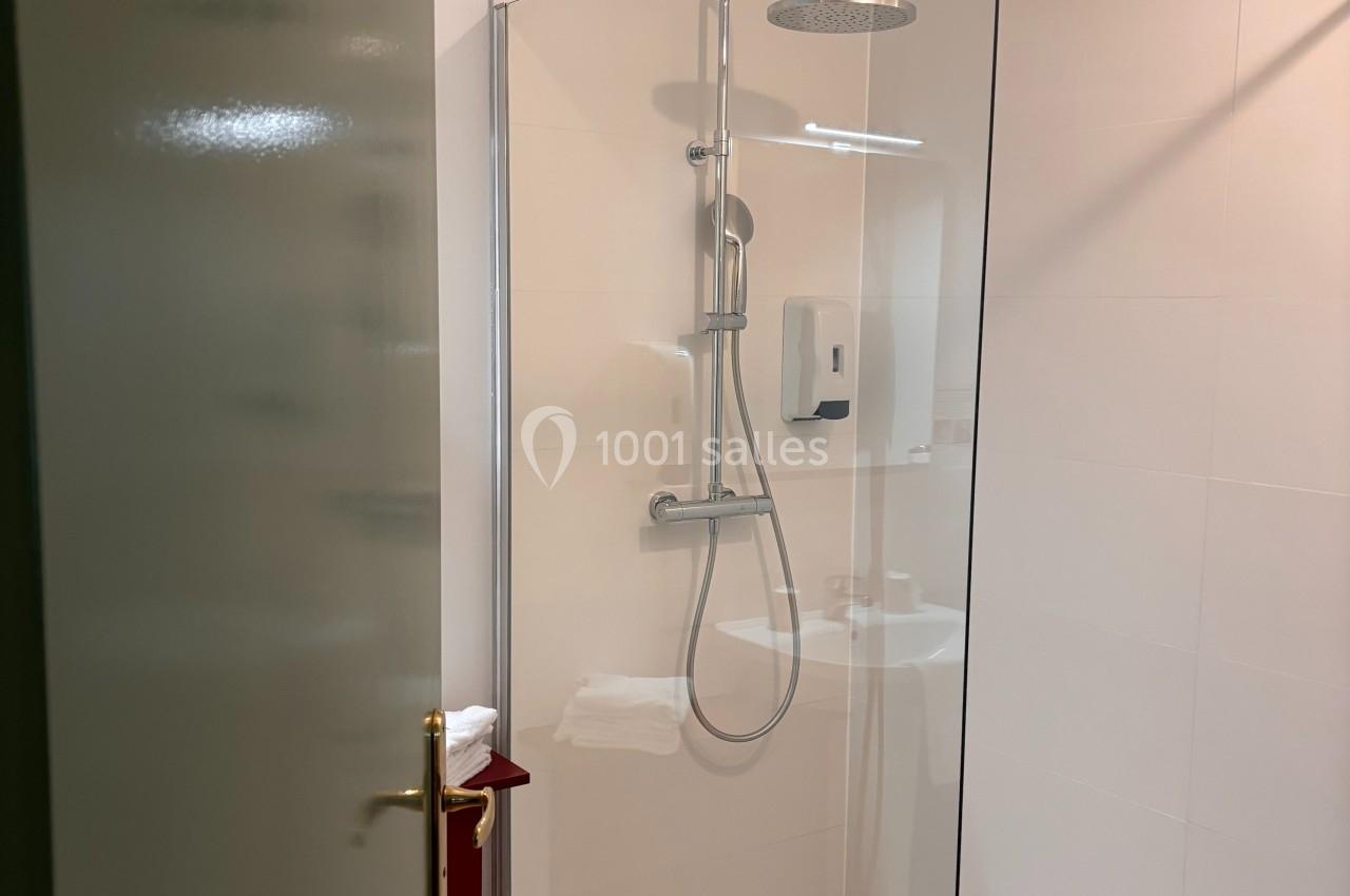 Douche moderne avec paroi en verre, pommeau de douche mural et sol en bois visible à l'extérieur.