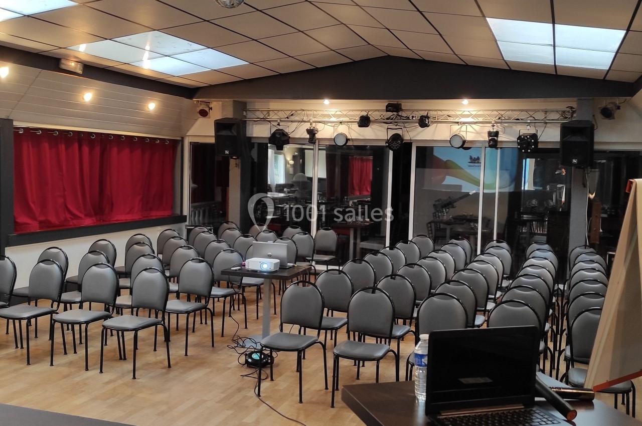 Salle de conférence équipée de chaises alignées, d'un projecteur, d'un tableau blanc et d'une scène avec éclairage.