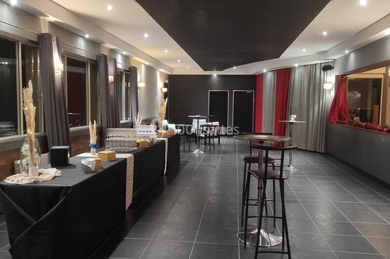 Salle moderne avec tables hautes, buffet dressé et éclairage tamisé, offrant un cadre élégant et épuré.