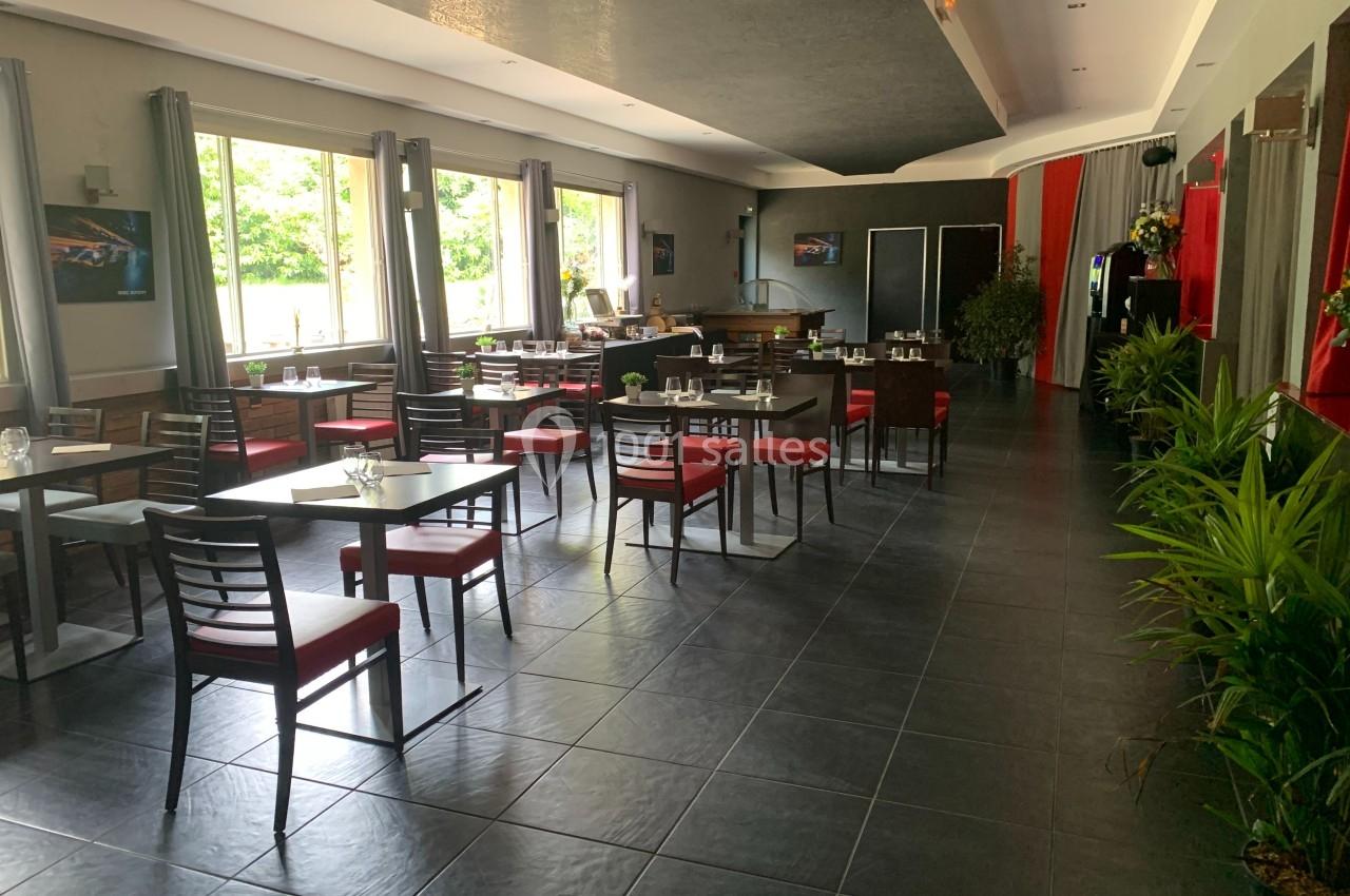 Salle de restaurant lumineuse avec tables et chaises alignées, grandes fenêtres et plantes décoratives.