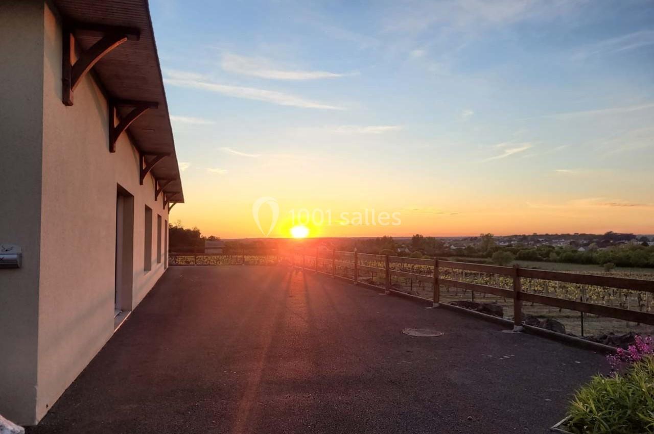 Coucher de soleil illuminant une terrasse asphaltée avec une maison à gauche et des champs à l'horizon.