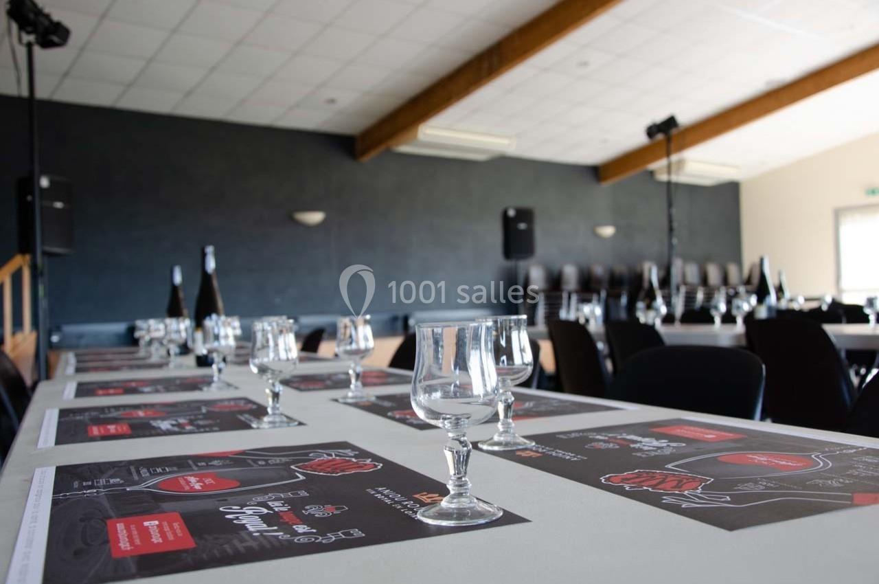 Salle de réception avec tables dressées, verres et menus, éclairée par une lumière naturelle.