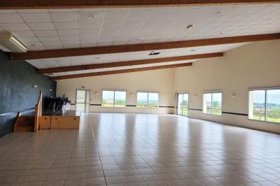 Vue d'un paysage rural avec un bâtiment moderne à gauche, des vignes et un château au loin sous un ciel dégagé.