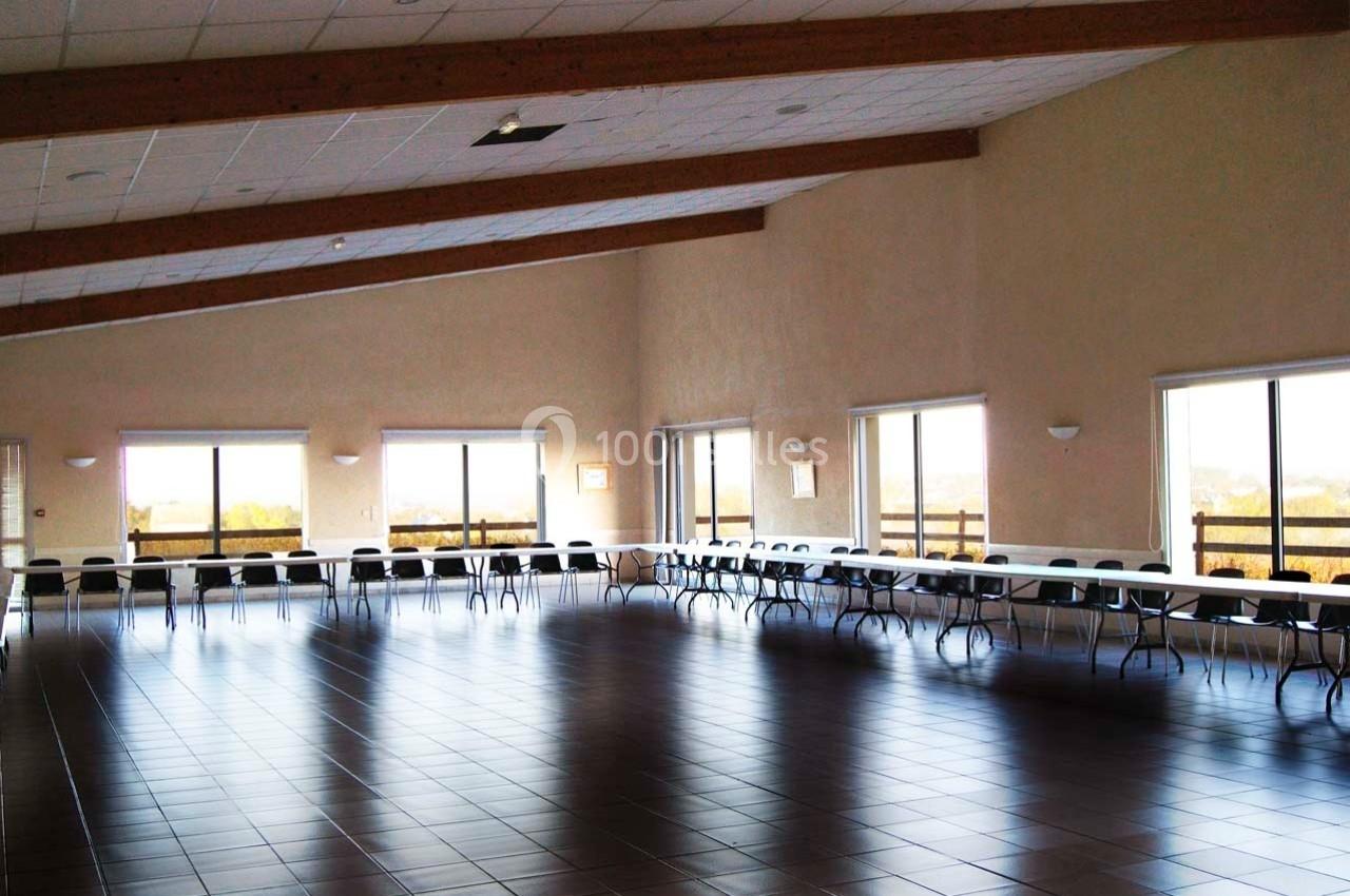 Grande salle lumineuse avec des tables et des chaises disposées en U, fenêtres donnant sur un paysage extérieur.