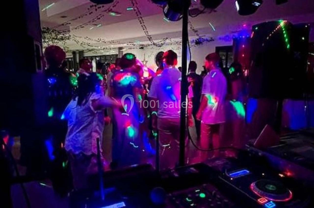 Personnes dansant sous des lumières colorées dans une salle sombre, avec une table de mixage au premier plan.