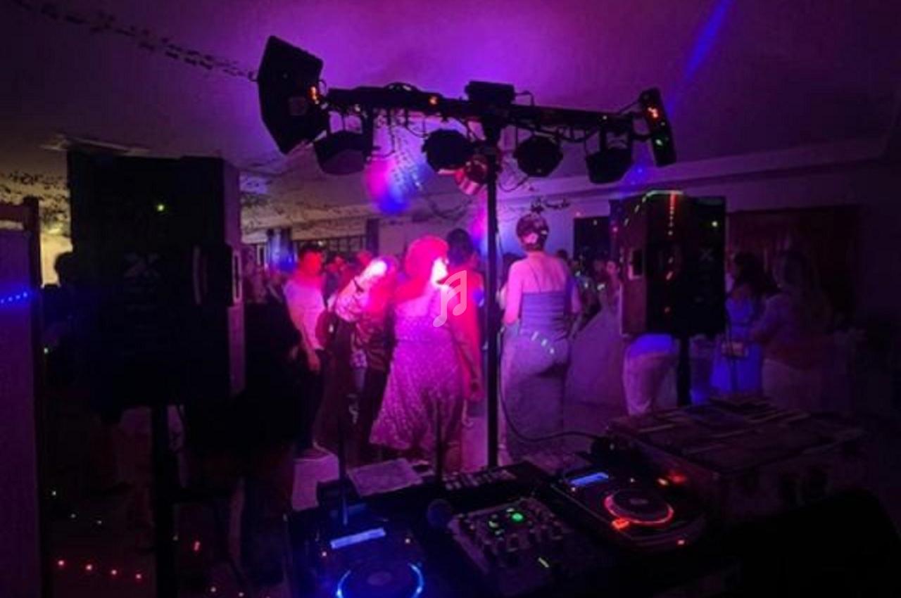 Des personnes dansent sous des lumières colorées près d'une table de mixage et d'enceintes dans une ambiance festive.