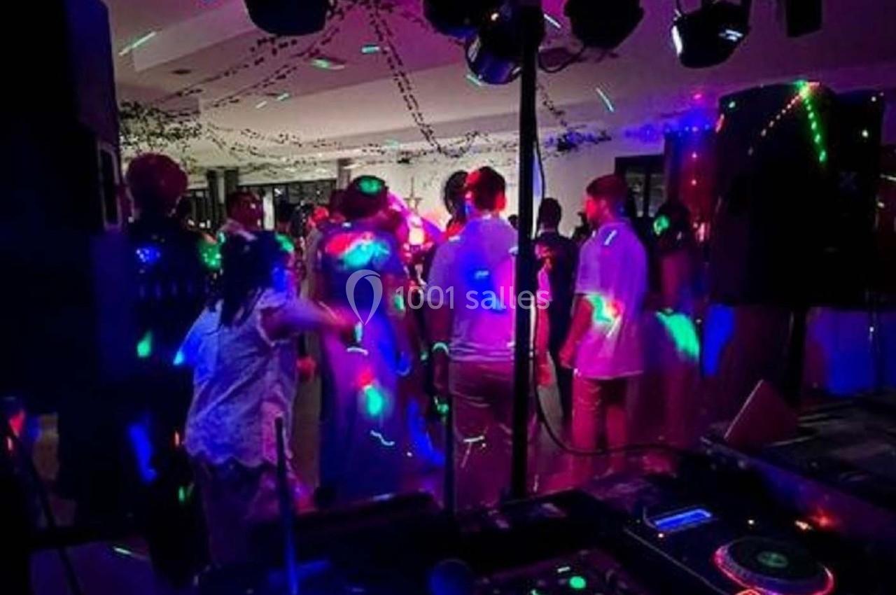 Des personnes dansent sous des lumières colorées dans une salle sombre, ambiance festive avec musique en arrière-plan.