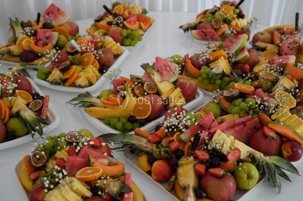 Plateaux garnis de fruits variés tels que pastèques, raisins, ananas, oranges et fraises, disposés sur une table blanche.