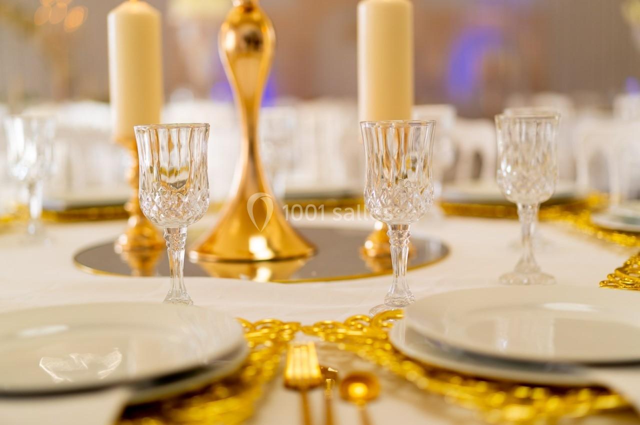 Table élégamment dressée avec assiettes blanches, verres en cristal, couverts dorés et bougies décoratives.