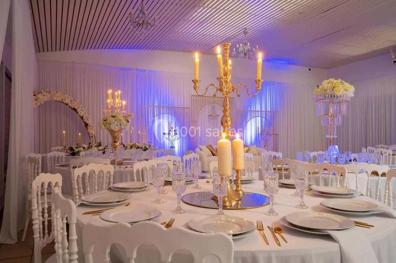 Salle de réception élégante décorée avec des chandeliers dorés, des fleurs blanches et des tables dressées.