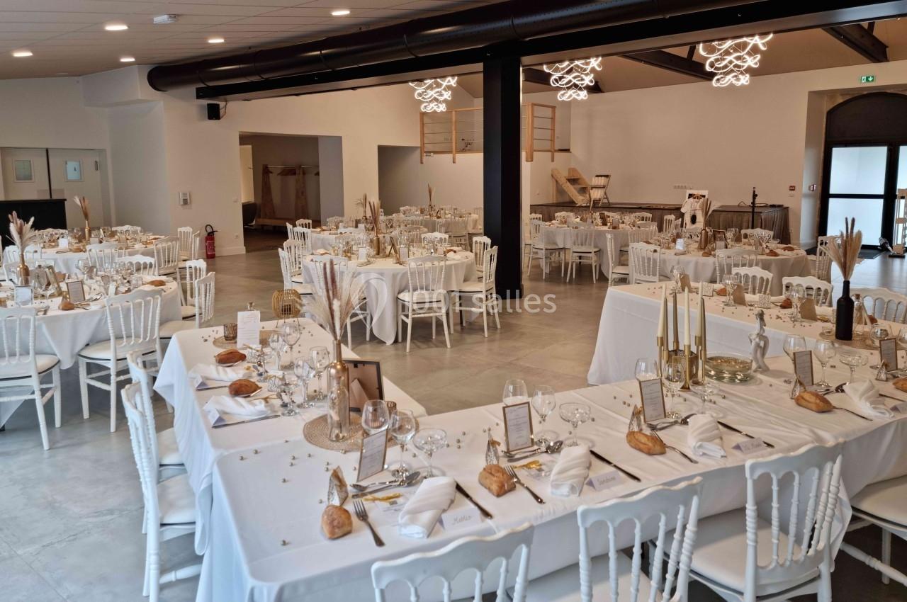 Salle de réception décorée pour un événement, avec tables dressées, nappes blanches et éléments de décoration élégants.