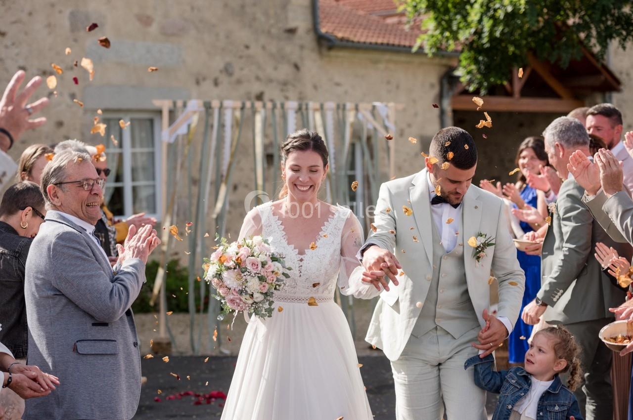 Un couple de mariés souriants sort sous une pluie de pétales, entouré d'invités applaudissant.