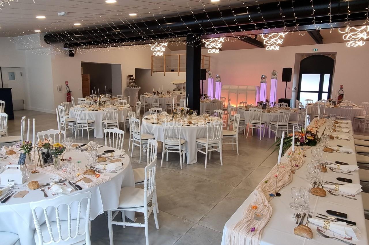 Salle de réception décorée avec des tables rondes et rectangulaires dressées pour un événement festif.