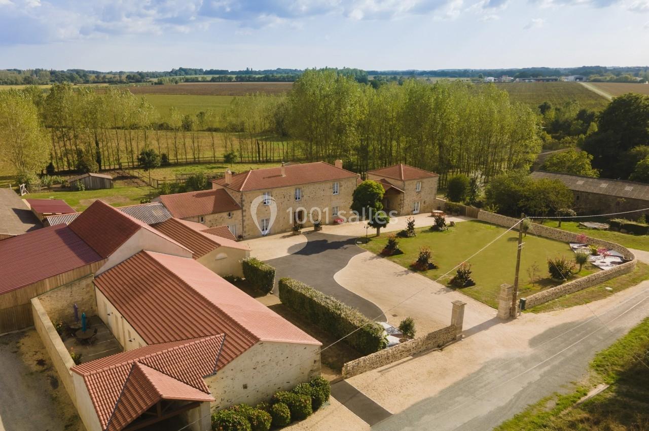 Vue aérienne d'une propriété rurale avec bâtiments en pierre, toits rouges, cour centrale et champs environnants.