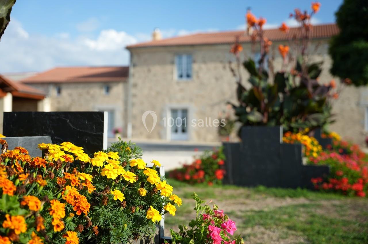 Massif de fleurs colorées devant une maison en pierre avec toit en tuiles, sous un ciel dégagé.